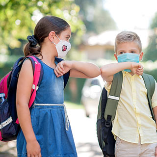 Two kids greet each other with an elbow bump while wearing face masks