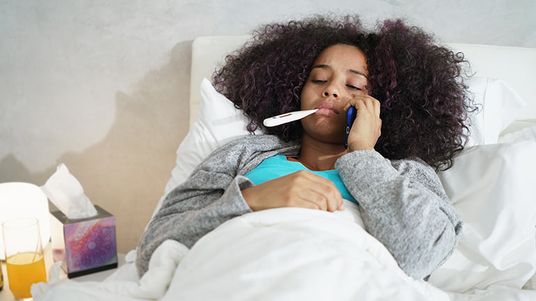 A girl at home in bed with the flu, taking her temperature